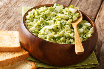 Summer homemade salad of ripe avocado with boiled eggs and green onions seasoned with yogurt closeup on the table. horizontal