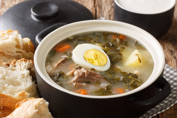 Ukrainian green borsch with sorrel, vegetables, meat and egg close-up in a pan on the table. horizontal