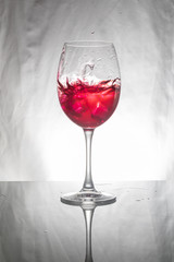 Glass with red liquid splashing with ice.