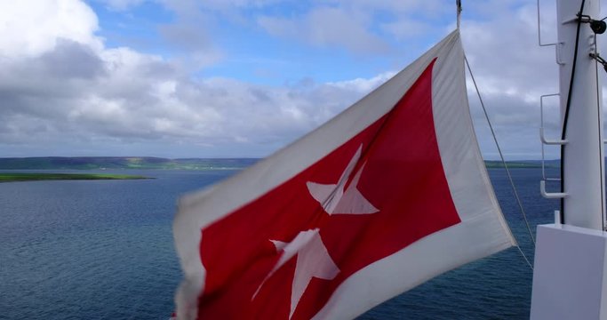 Close up of white Maltese cross on red background flag, the national flag of Malta and civil ensign flown by cruise ship, isolated against the blue sky waving in a breeze