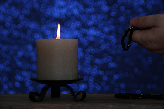 female hands with beads folded in prayer to God, candle burns with a bright flame, religious concept of prayer, sins, remorse, guilt, requests