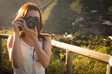 Joven fotógrafa de pelo rojo a contraluz tirando fotos en el campo.