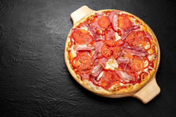 VESUVIO pizza on a black background, tomato-based with mozzarella, ham, bacon, tomatoes and bell pepper