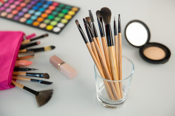 professional set of make-up brushes in a glass on background of cosmetic bag and other make up products