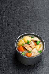 Stewed pork with vegetables in small clay pot on black stone background