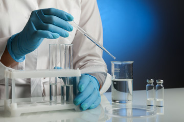 medical scientist drops the liquid with a pipette into a lab glass beaker close up. doctor works with lab glassware close up. Biochemist`s hands in blue gloves are conducting chemical experiments