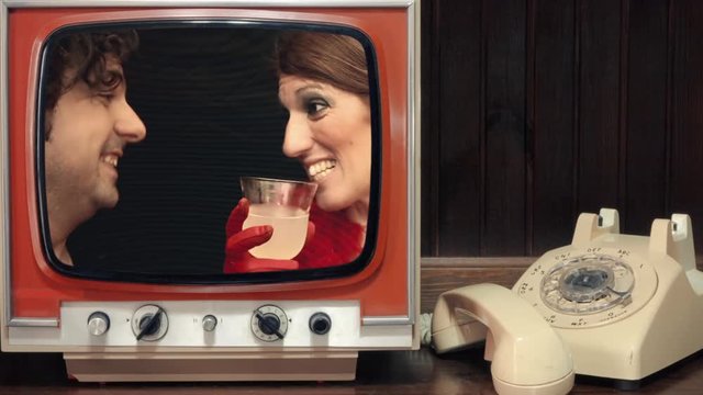 A room with a rotary phone and a vintage tv showing a timelapse: a funny couple at a party, a talkative self-confident woman and a shy bored annoyed man. Comedic shot.
