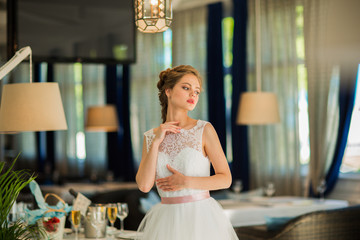 Portrait of pretty young blond bride with hairdressing in white dress at restaurant