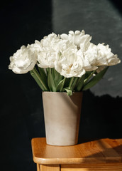 Белые тюльпаны в  вазе  на деревянном столе на темном фоне. Много цветов, букет с дневным светом.