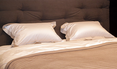 Close-up of a new brown-colored blanket with decorative pillows, fabric headboard in bedroom in sample model of hotel or apartment