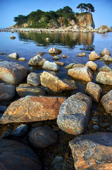 Rocky high island in the ocean. Rocky high island in Orlik Bay in the Sea of Japan. In the foreground are stones and clear water. Far East.