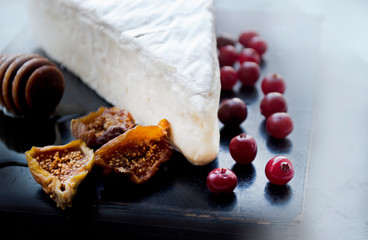 Brie cheese and honey, cranberries and dried figs on a black kitchen board.