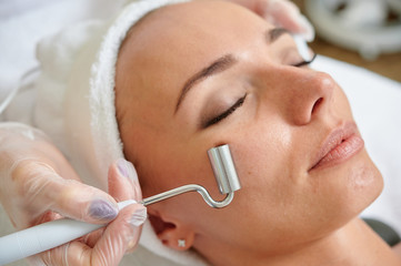 Female receiving electric facial treatment by cosmetologist wearing gloves professional services.