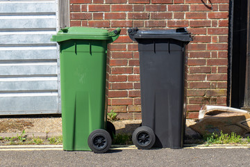 Obraz premium a green and a black wheelie bin side by side on a street