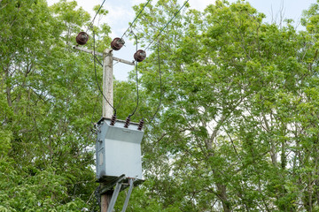 Electric power cables together with a large transformer seen attached to a heavy duty wooden pole...
