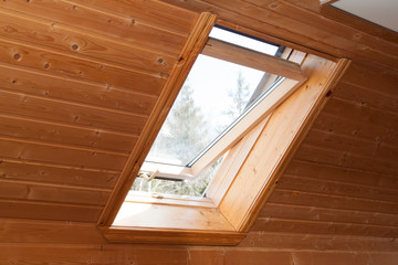 Open dormer window in wooden house in the attic. Room has sloping ceiling made of natural...
