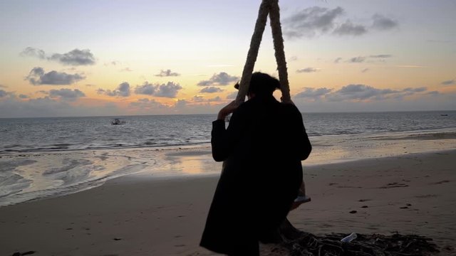 A young woman on a homemade rope swing at a beautiful Brazilian beach during sunrise in Joao Pessoa Brazil