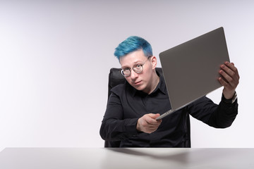 Young caucasian man is showing his laptop, raising it up with both hands and looking quizzical into a camera, studio photo