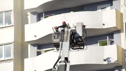 Aerial platform fire truck raises firefighters in a protective basket to extinguish a fire in a multi-story high-rise building, fireman
