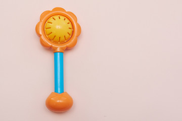 Plastic toy rattle in bright yellow color with a blue handle. Plastic Retro Rattle. Baby toys on pink background. Flat lay. Copy space.