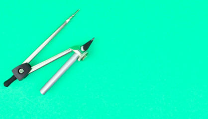 Silver color drawing compass attached to a pencil placed on top of a light blue background