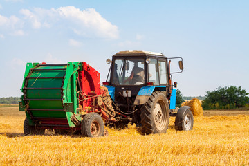Fototapeta na wymiar tractor makes big straw roll on yellow field at summer day