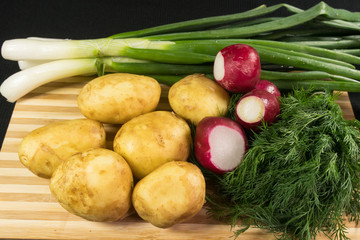 Young potatoes, radish, green onions, dill on a wooden board, black background