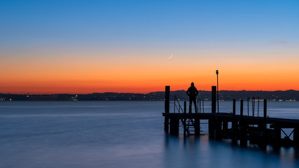 A man silhouette standing on wooden pier lonely at the sea with beautiful sunset. lsunset seascape at a wooden jetty.
