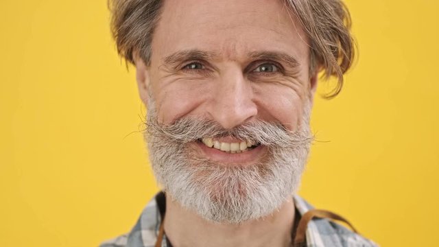 Senior pleased man isolated over yellow background looking camera winking