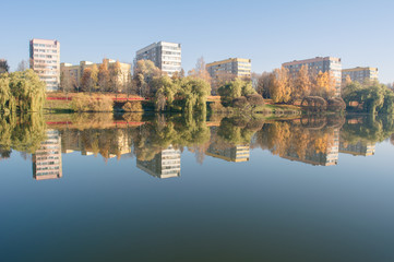 panel houses stand on the shore and are reflected in the water of a smooth and calm river