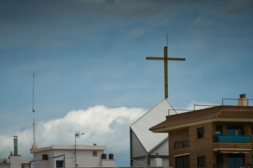The cross at the top of the modern church tower inside a city