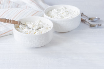fresh cottage cheese in white bowls on the table close-up. background with cottage cheese in bowls, napkin and spoons. cottage cheese in bowls close-up.
