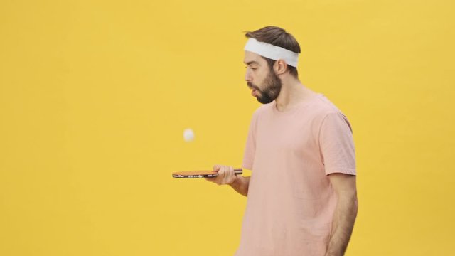 A focused young athletic man in sportswear is playing ping-pong isolated over a yellow background in studio