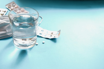Coronavirus prophylaxis with surgical masks and gloves. Medical mask, pills, drugs, water in a glass. Light blue background. Free space for text.