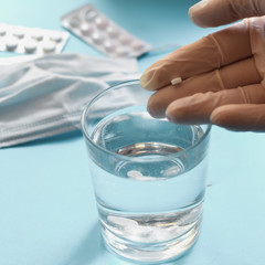 Coronavirus prophylaxis with surgical masks and gloves. Medical mask, pills, drugs, water in a glass. Light blue background. Free space for text. Hands in gloves.