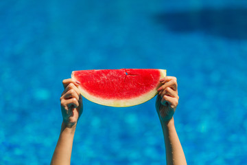 Girl holds a slice of slice of watermelon in the pool. Resting in the pool and eating sweet juicy fruits.