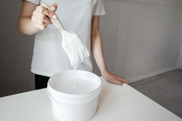 Female hand holding brush over the can with white paint against neutral background. Repair concept.