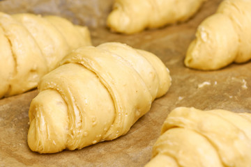 Producing of classic croissants from rolled layered dough. at home. Raw classic crescent rolls on a baking paper. Traditional french pastry