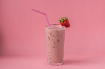 Strawberry milkshake with a pink straw and strawberries on a glass on a pink background. Healthy food and diet concept
