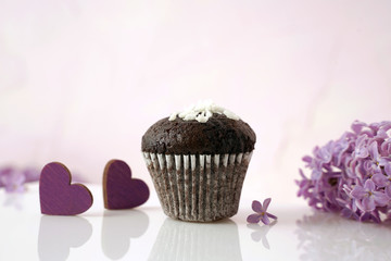 chocolate cupcake, lilac flowers and hearts on the surface with reflection