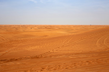 Red sand dunes in Sharjah, UEA during a sunny day. A lot of sand and plenty of tire marks and some footprints since there has been tourists doing dune bashing, walking and enjoying the Middle East.