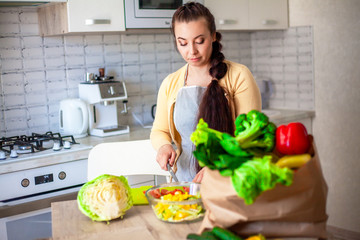 Young brunette woman making healthy food on the dinner table in the kitchen. Female cooking fresh vegan salad with green vegatable