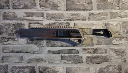 Disassembled stationery knife, blade replacement in knife on a brick wall background.