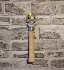 Manual glass cutter with a wooden handle on a brick wall background.
