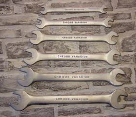 Set of open-end wrenches under the nuts on a brick wall background. .