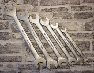 Set of open-end wrenches under the nuts on a brick wall background. .