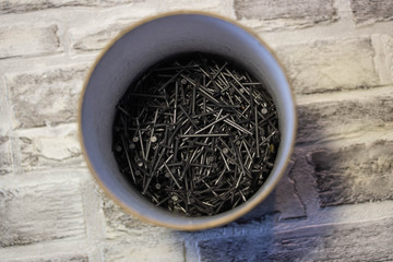 Black nails in a jar on a brick wall background.