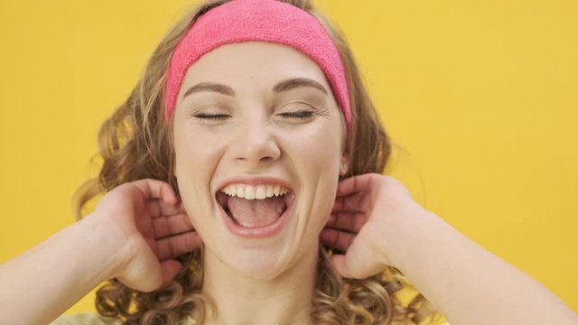 A happy pleased young athletic woman in sportswear is laughing while looking to the camera isolated over a yellow background in studio