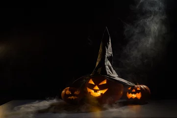 Foto op Plexiglas Spooky orange pumpkins for Halloween stand in a row on a dark background. Jack O Lantern in a witch hat. Mystical fog creeps on the ground. Trick or treat. © Михаил Решетников