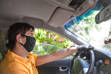 Young man in black mask driving a car and wearing yellw t-shirt, headphones and gloves. Tje hands of man holding the wheel of a vehicle. Safety of virus concept